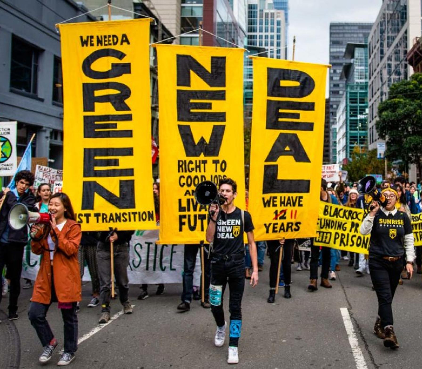 
        Young people at a climate march, 
        carrying a banner that says “Green New Deal.”
      